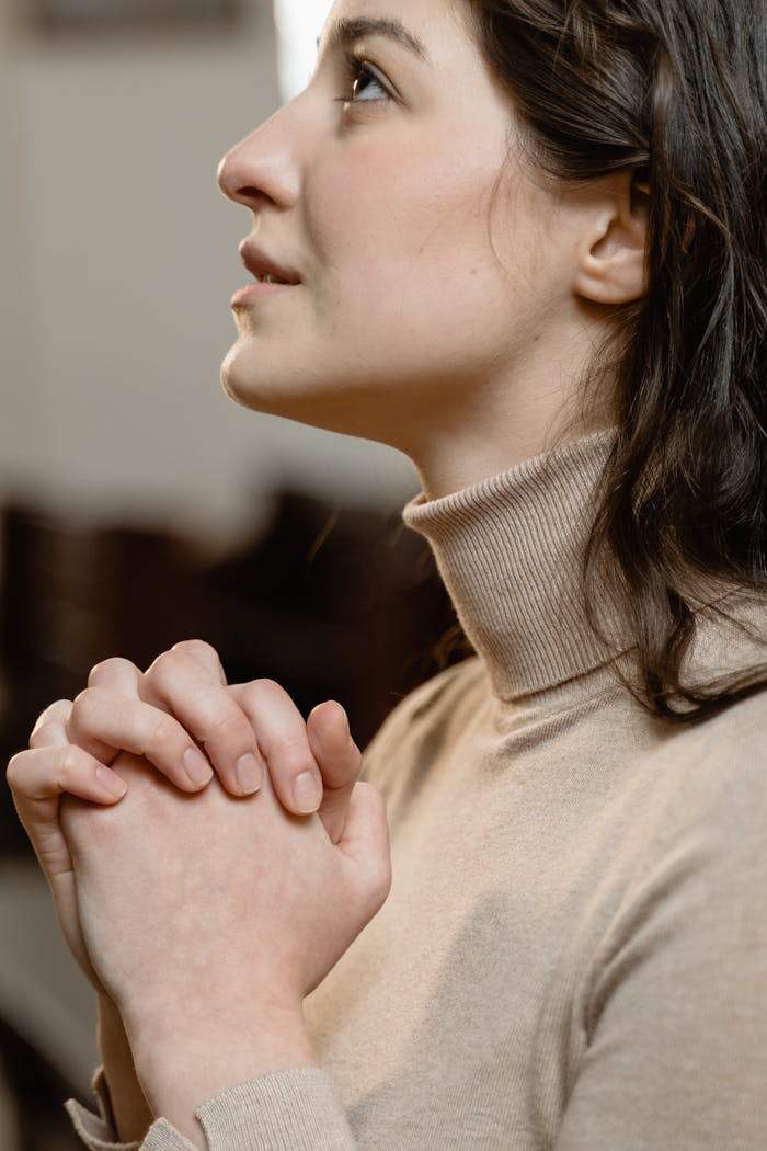 Woman in a turtleneck praying with clasped hands, serene expression.